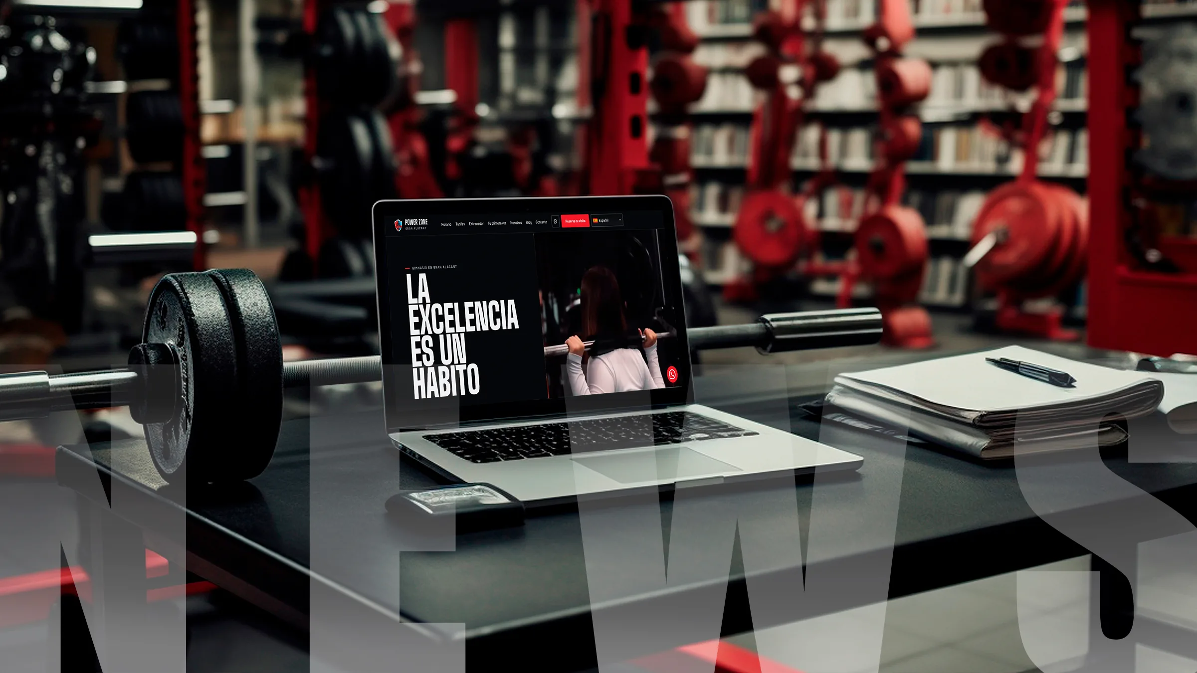 Portátil con la web de Power Zone sobre una mesa de gimnasio, junto a una barra con discos y el rótulo News: blog del gimnasio en Gran Alacant
