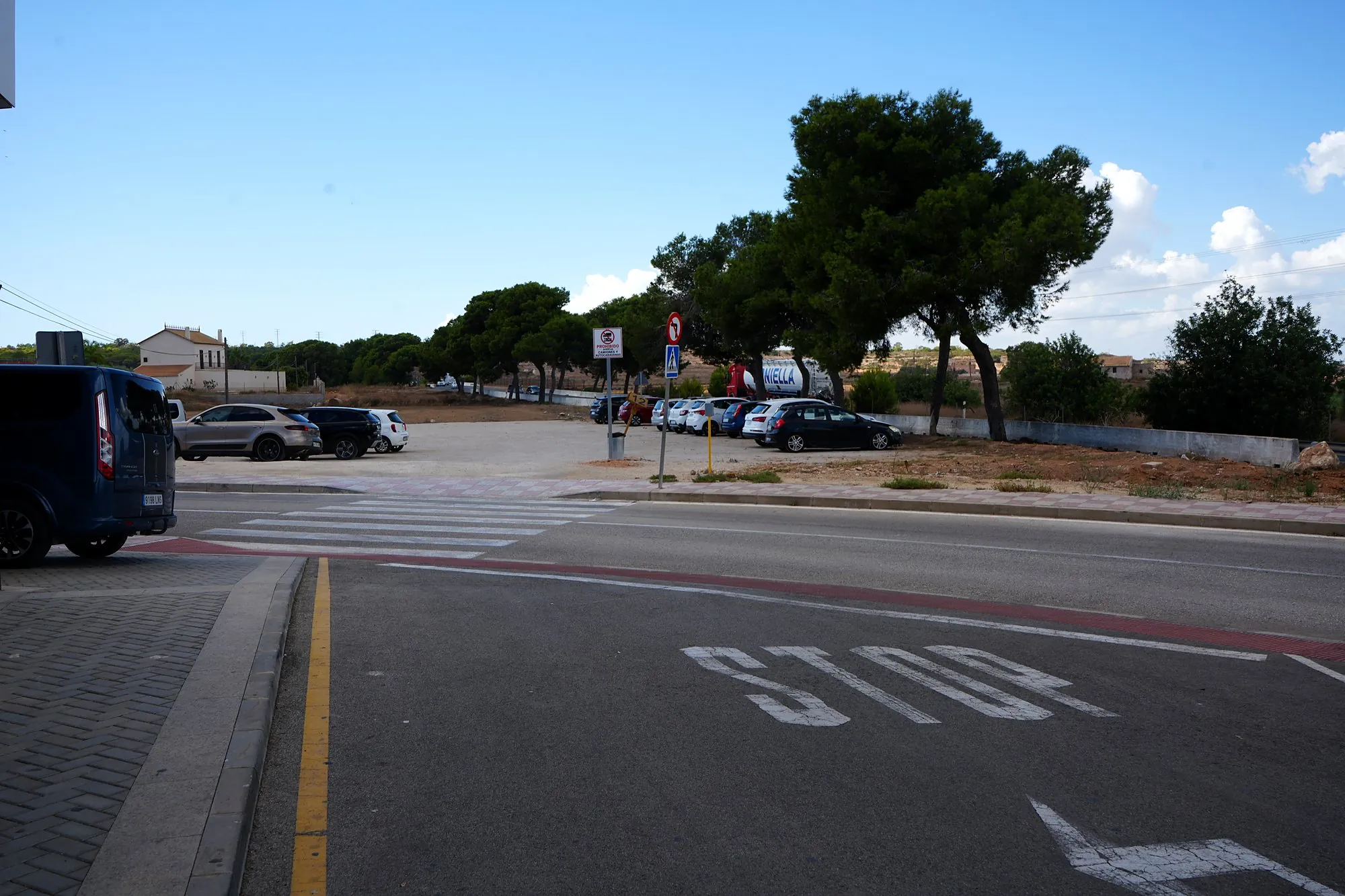 La calle frente al gimnasio, con aparcamiento y pinos al fondo