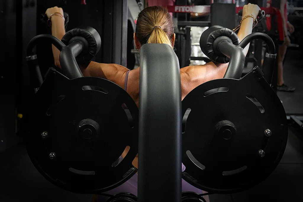 Una mujer entrena hombro en una máquina, vista de espaldas